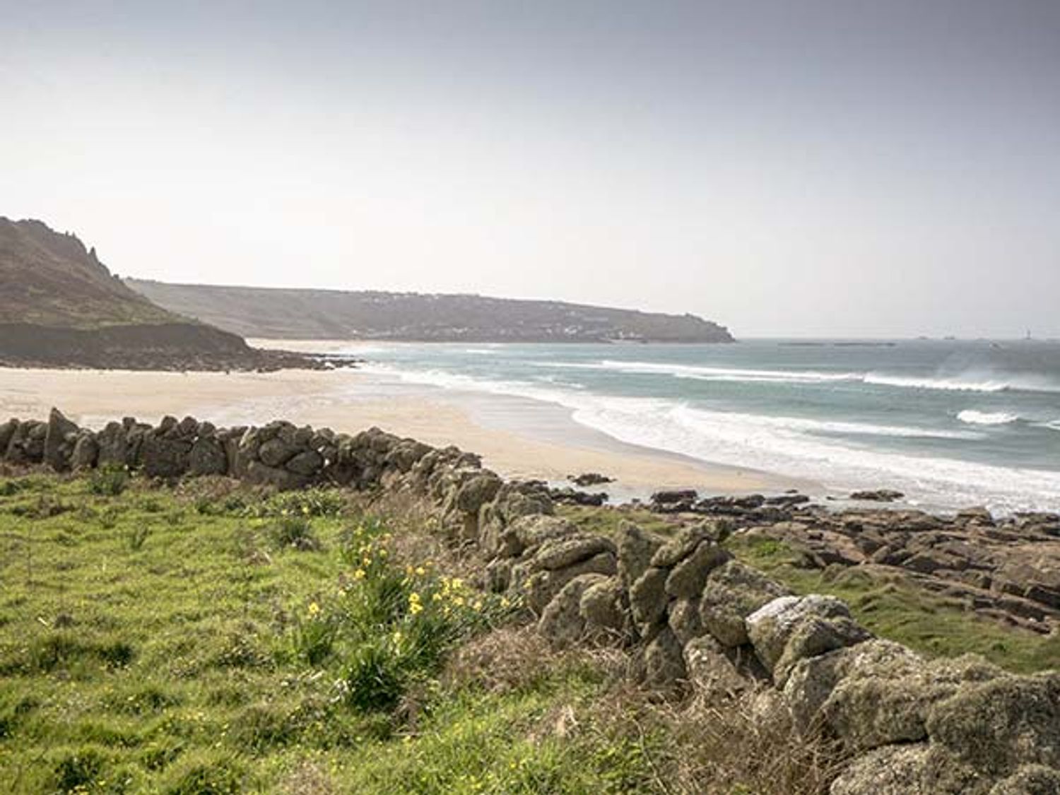 A coastal landscape with a stone wall grass and flowers by the sea at Brook House in Sennen Cove near St Just