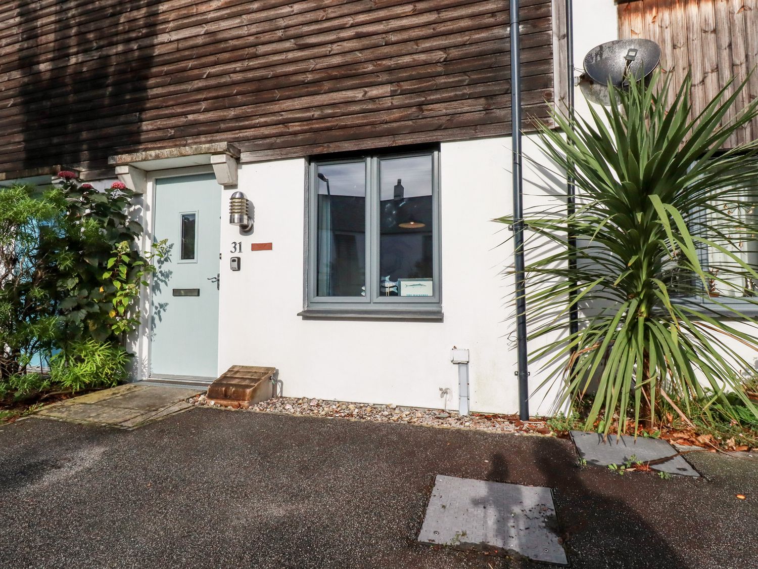 The exterior of a house showing a light blue door with a window next to it and plants on either side at The Mackerel in Charlestown