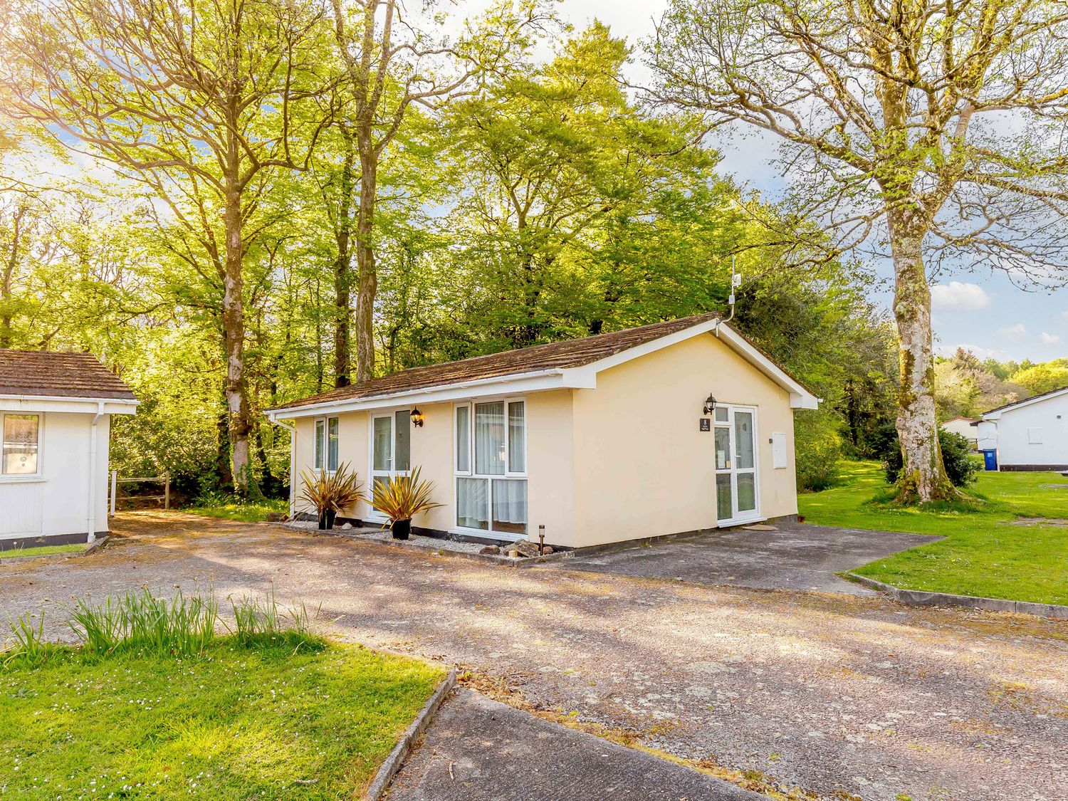 A single-story house with windows and doors surrounded by trees and grass at Brook Cottage Rosecraddoc Lodge near Liskeard