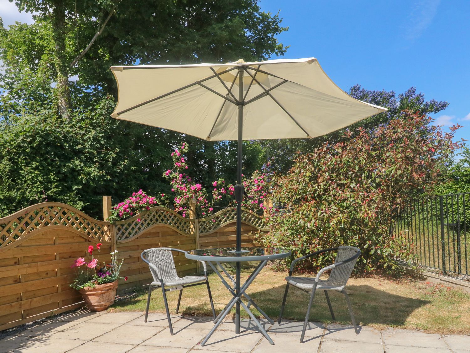 A patio with two chairs a glass table and an umbrella next to a wooden fence with flowers at Jacks Nest in Ash Mill near South Molton