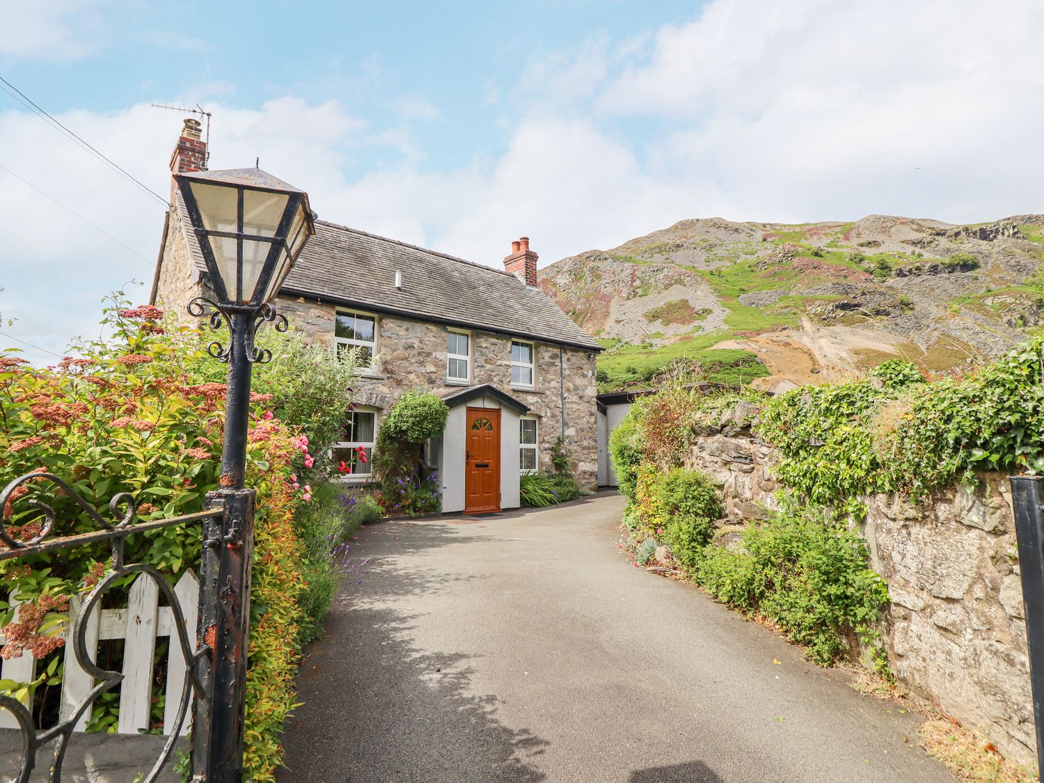 A stone house with a brown door and windows along a driveway with a lamppost and plants at Bodywen in Llangynog