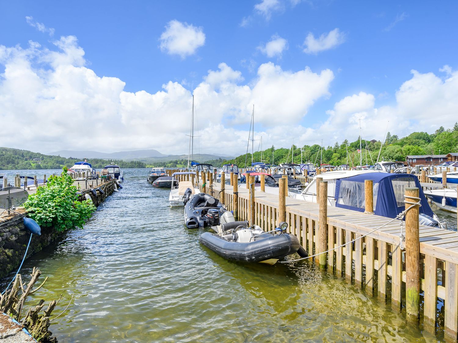 A dock with boats moored on a lake with hills and trees in the background at Claife View Lodge in Troutbeck Bridge