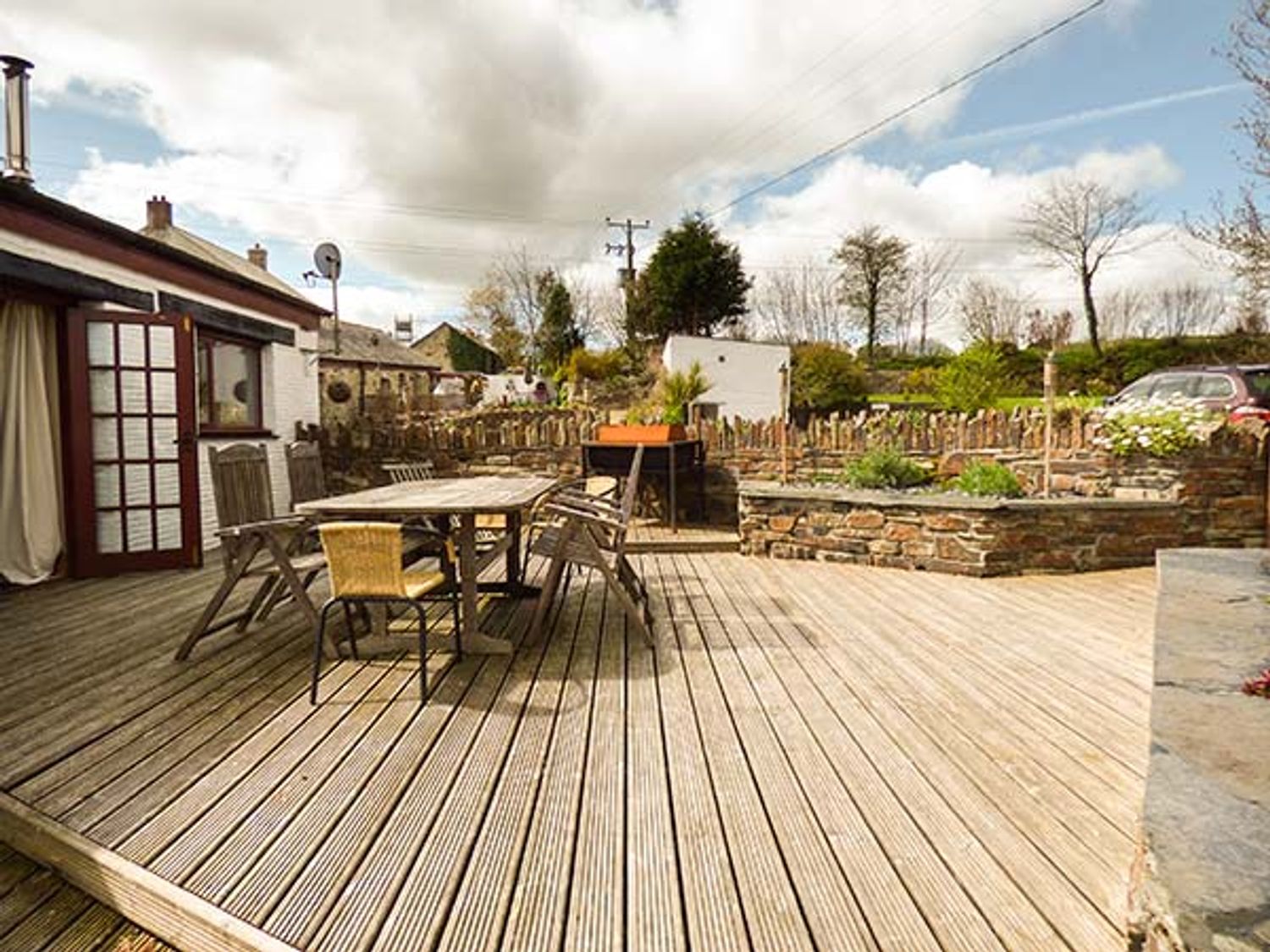A wooden deck with a table and chairs outside a house at Kingfisher Barn in East Taphouse