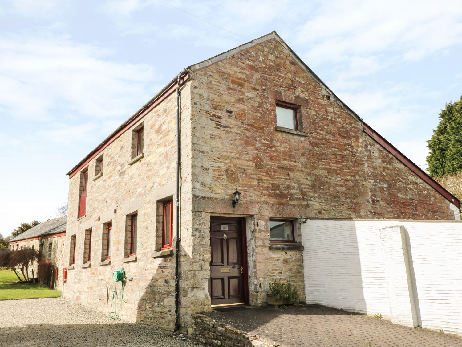 A stone building with red framed windows and a wooden door at Kingfisher Barn in East Taphouse