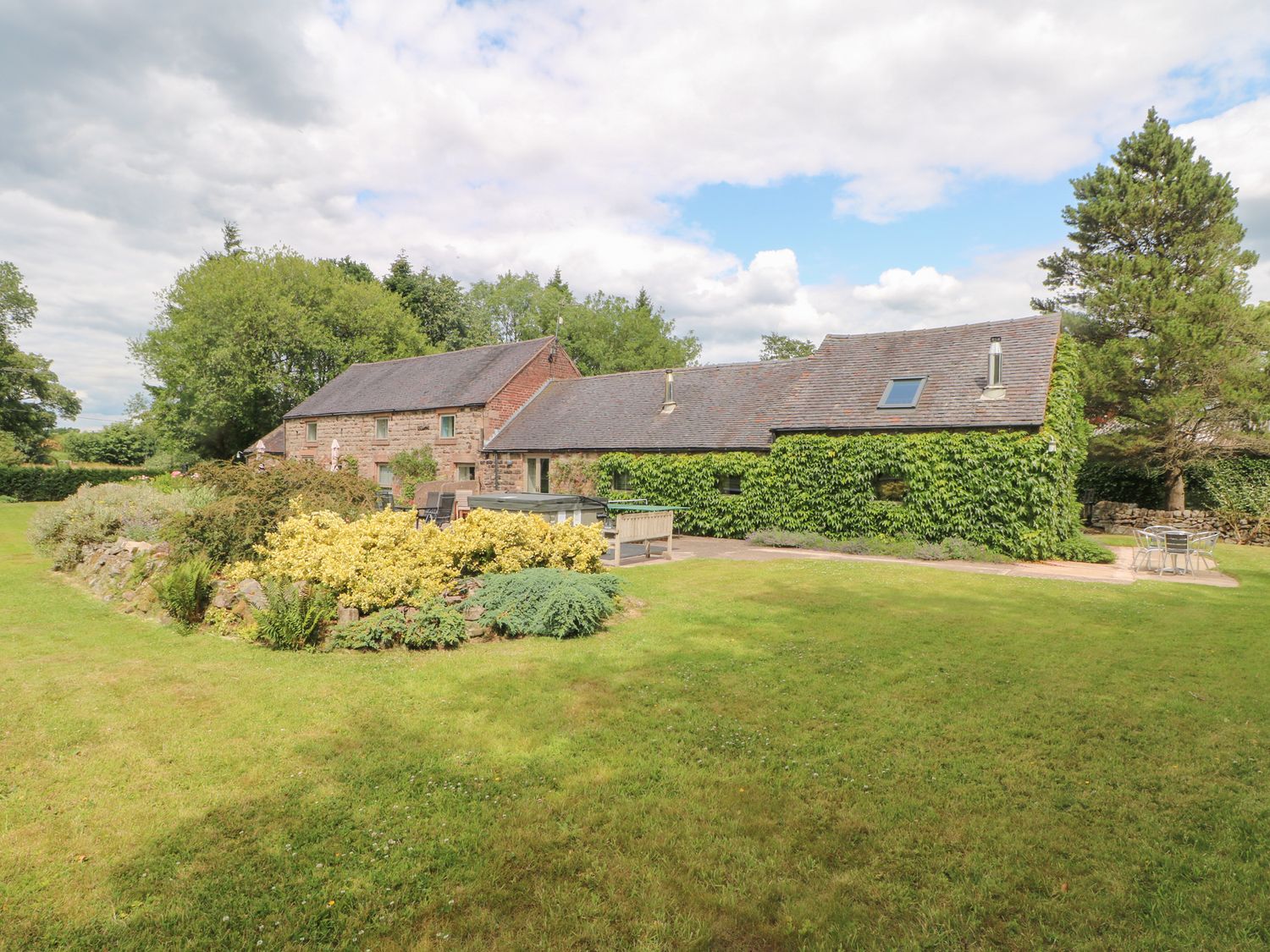 A garden with a building and seating area at Lee House Cottage in Cheddleton