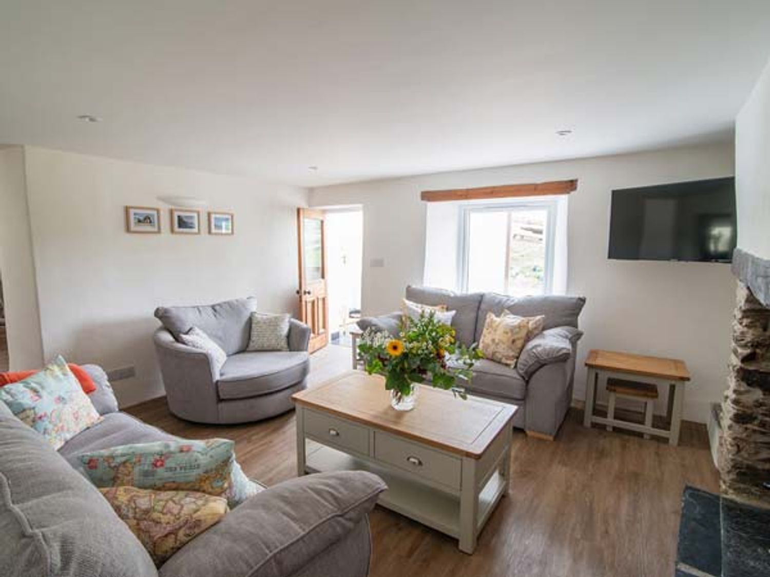 A living room with gray sofas a wooden coffee table with flowers and a wall-mounted TV at Five Elements Cottage in St Agnes