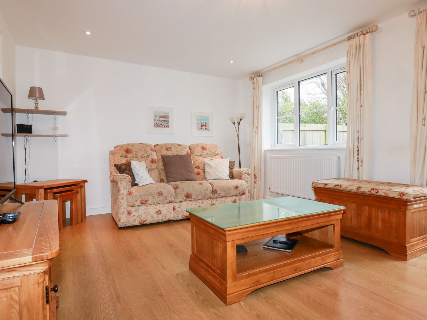 A living room with a floral sofa a wooden coffee table with glass top and a wooden chest with cushions at 4 Trevanson Mews in Newquay