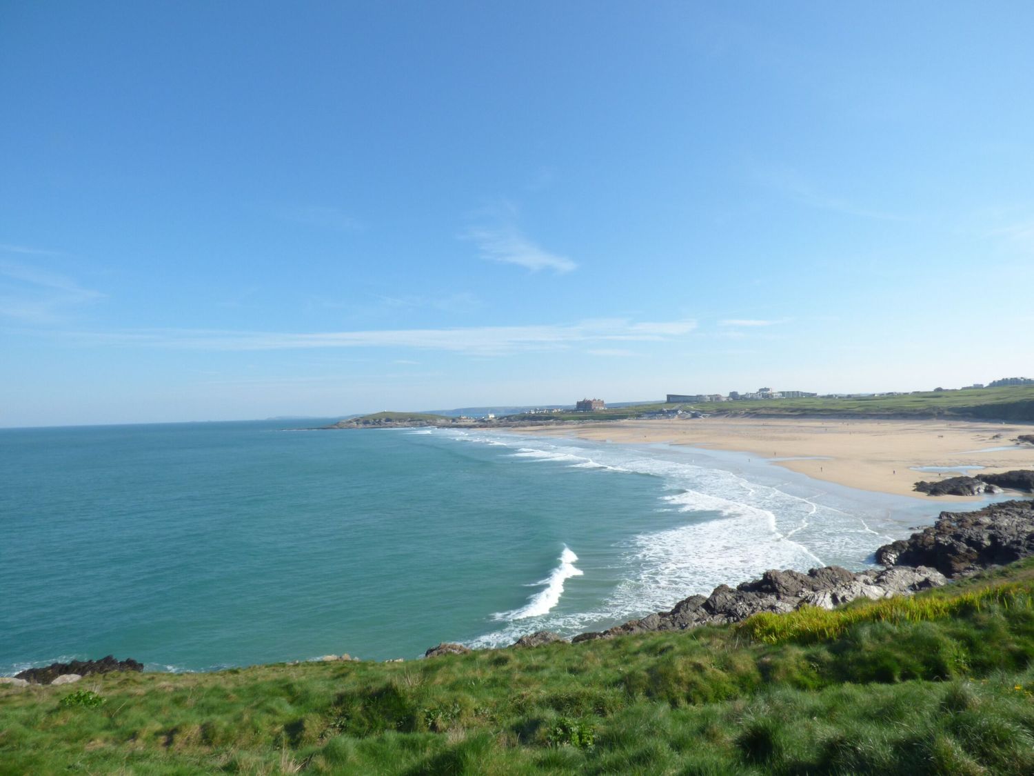 A coastal view with a beach sea and grassy cliffs at 4 Trevanson Mews in Newquay