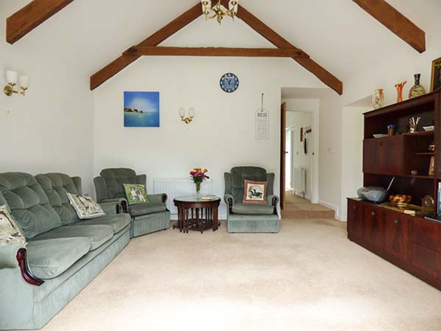 A living room with green sofas wooden beams and a wooden cabinet at Shepherds Rest in Jacobstow near Bude