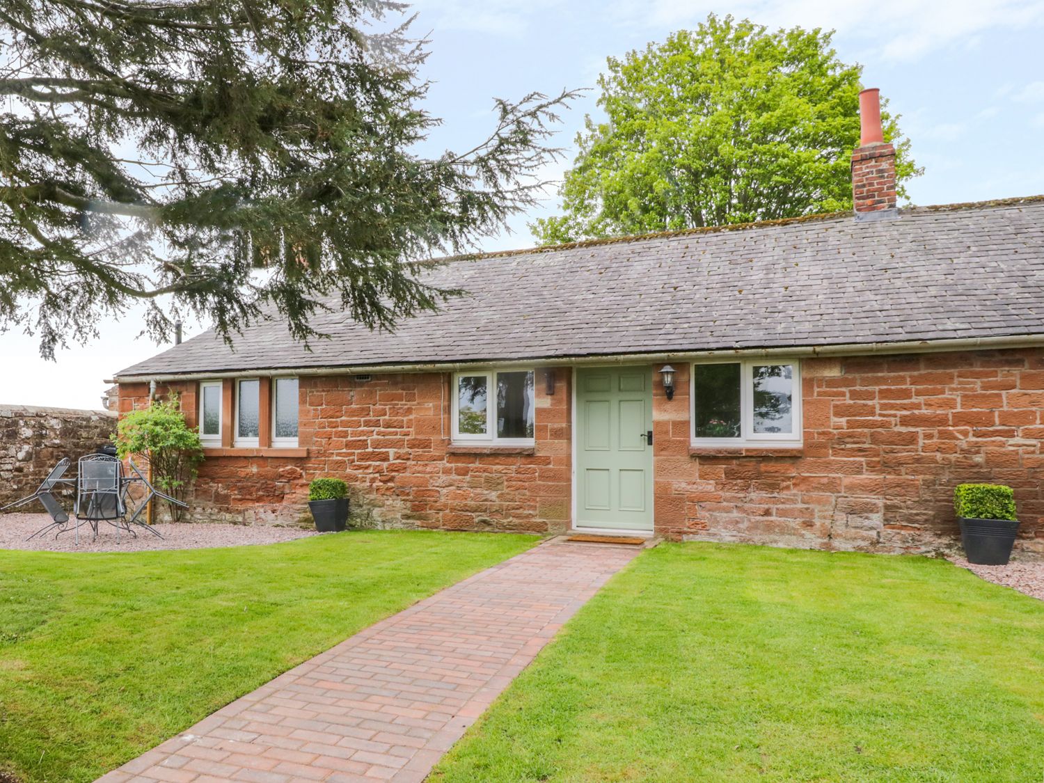 A brick cottage with green door and windows a paved walkway and outdoor seating area at Berrymoor Cottage in Corby Hill