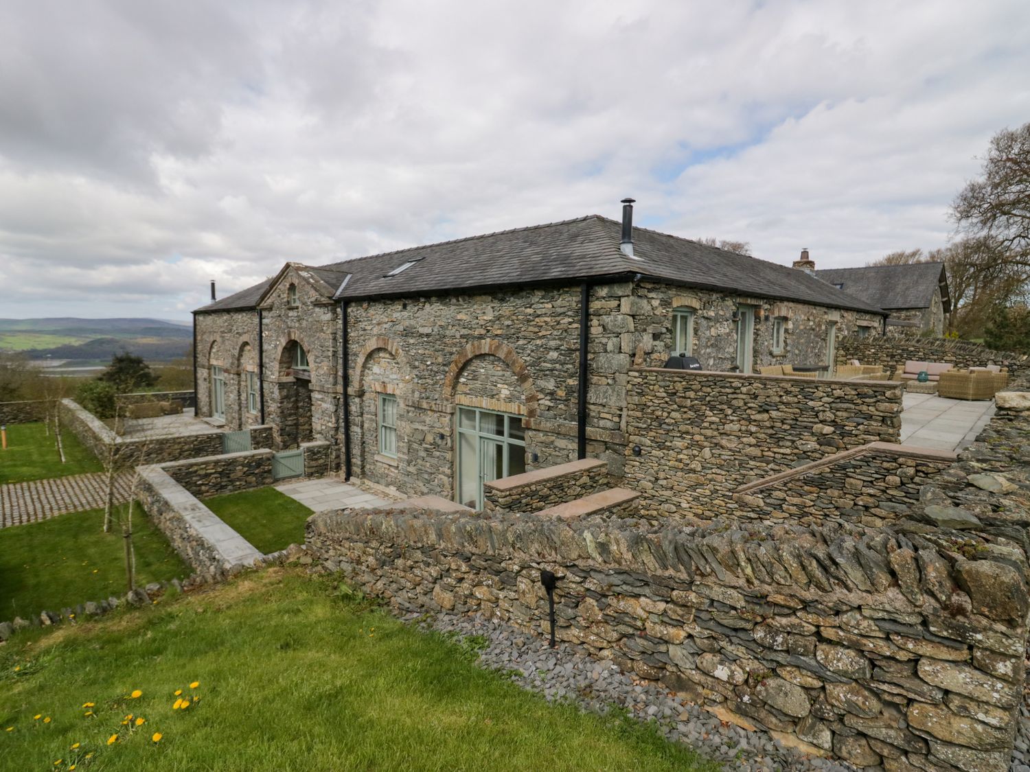 A stone house with stone walls and grassy lawn in a rural landscape at Rowan Cottage in Backbarrow near Newby Bridge