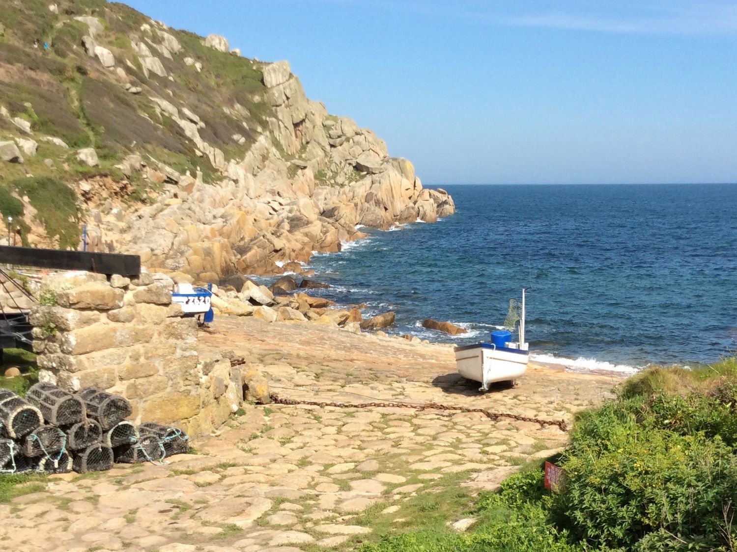 A small white boat on a rocky shore with lobster pots and a stone wall near the ocean at 14 Boscaswell Downs Pendeen near St Just