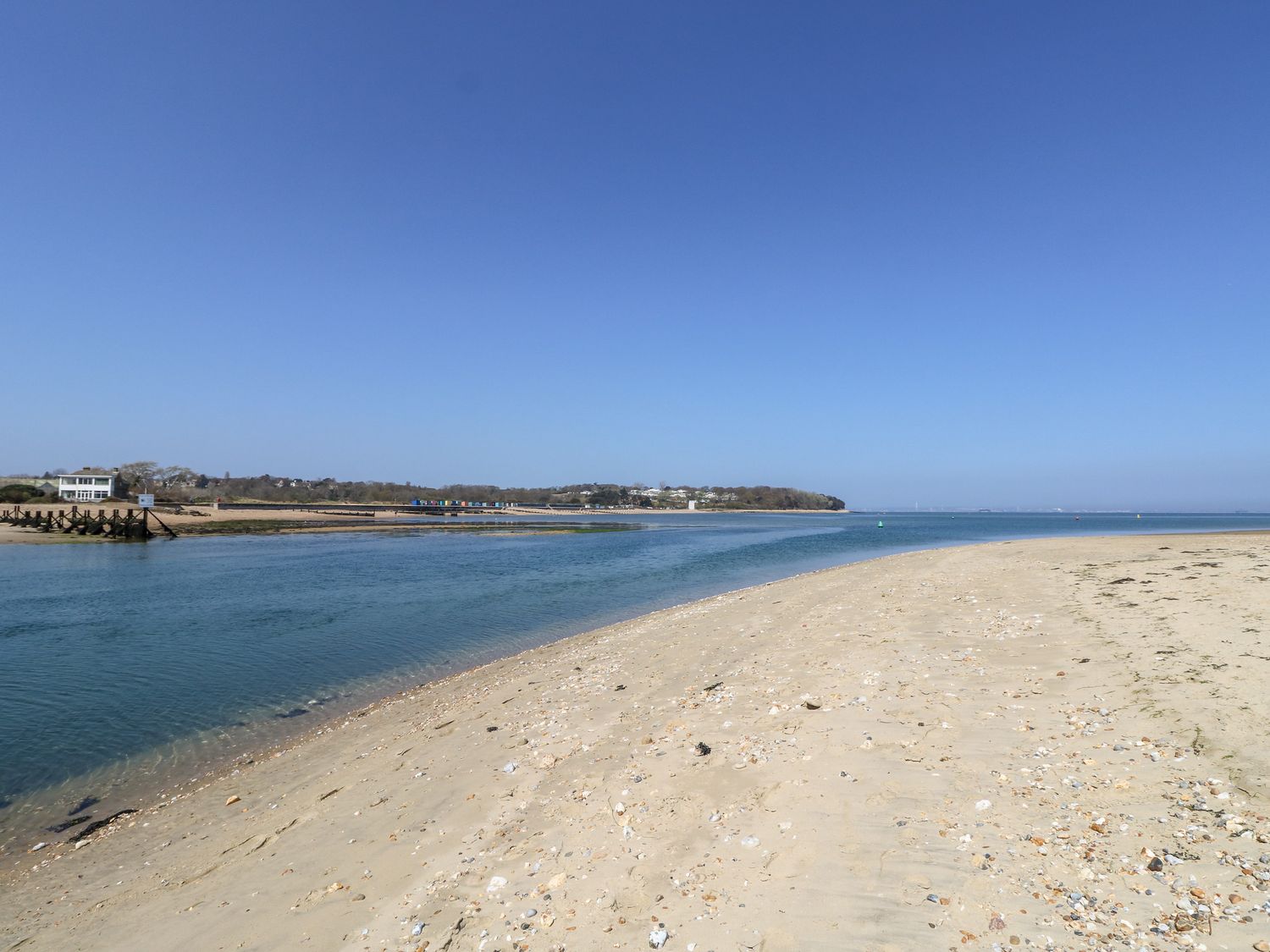 A sandy beach with a body of water and houses in the distance at 5 The Nab House in Bembridge