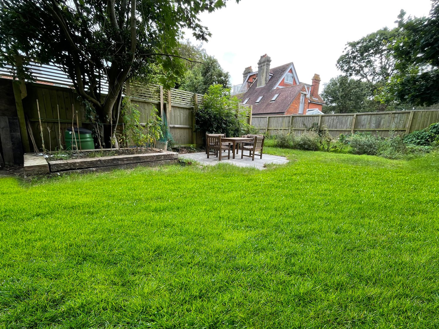A garden with a wooden table and chairs on a patio near a raised planting bed in the backyard of a house at 5 The Nab House in Bembridge