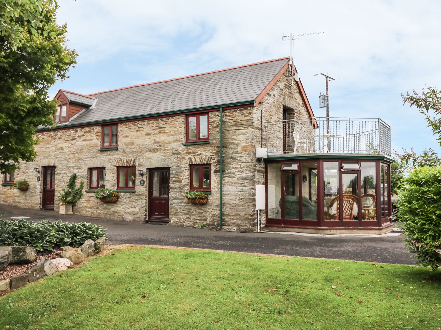 A stone cottage with glass conservatory and balcony overlooking a lawn at Oak Cottage in Bryngwenith near Newcastle Emlyn