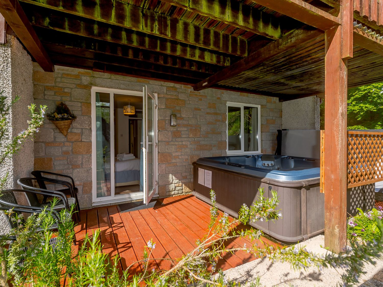 A patio with a hot tub two chairs and open doors leading to a bedroom at Brookside in Honicombe Manor near Gunnislake
