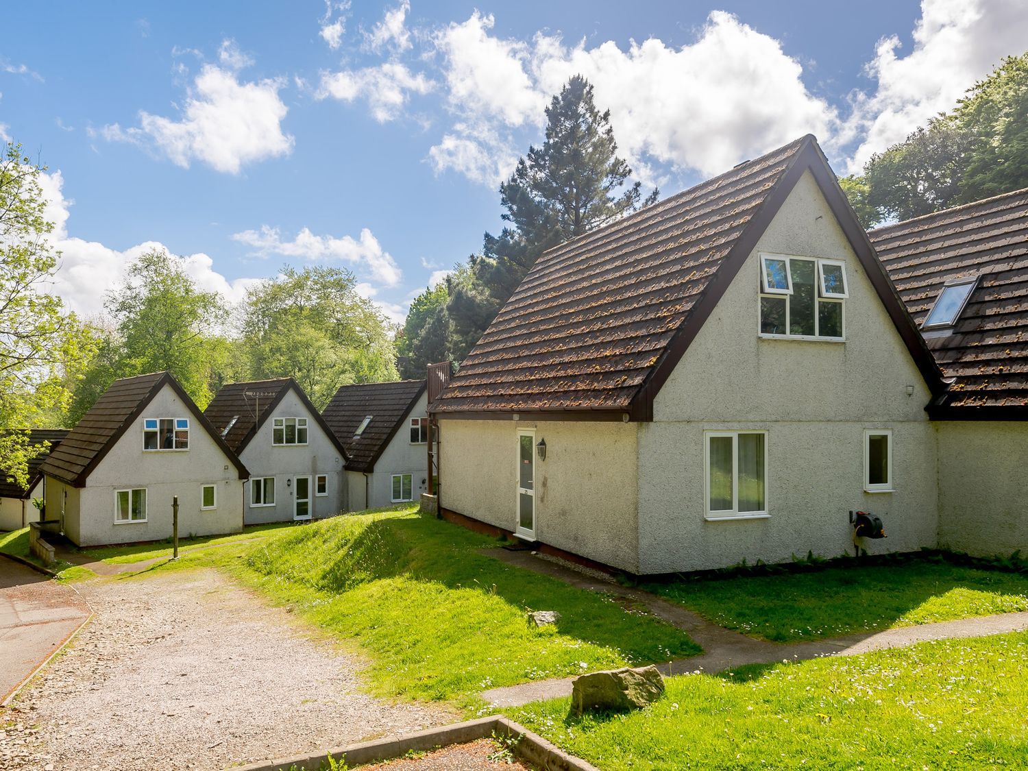 A group of houses with pitched roofs and green lawns under a blue sky at Brookside in Honicombe Manor near Gunnislake
