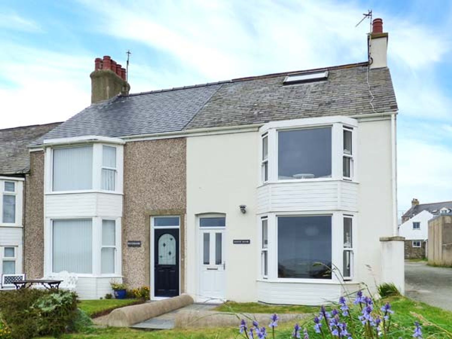 A semi detached house with two bay windows and a small garden with flowers at Sandy Bank in Rhosneigr