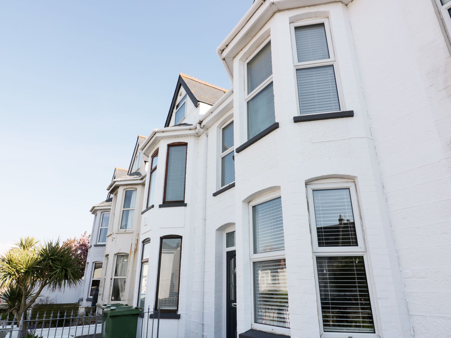 A row of white terraced houses with bay windows and a green trash bin in front at The Salt House in Newquay
