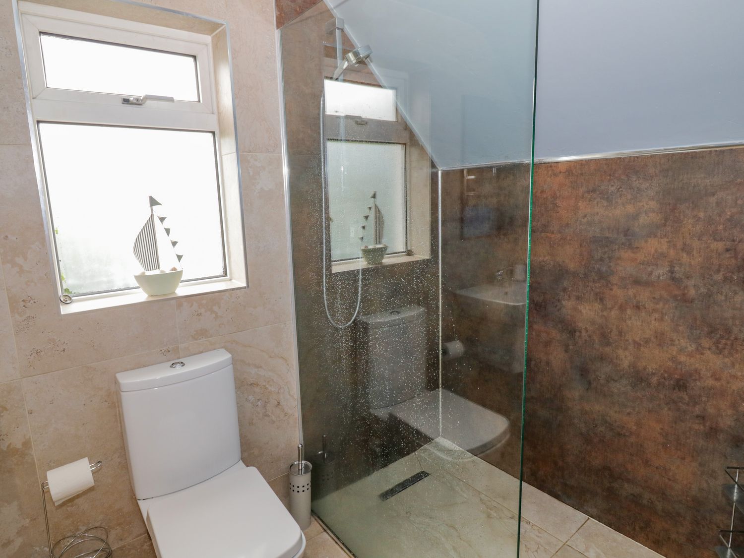 A bathroom with a toilet and a shower area with a glass partition and a window at Nathaniel's Cottage in Kirkcudbright