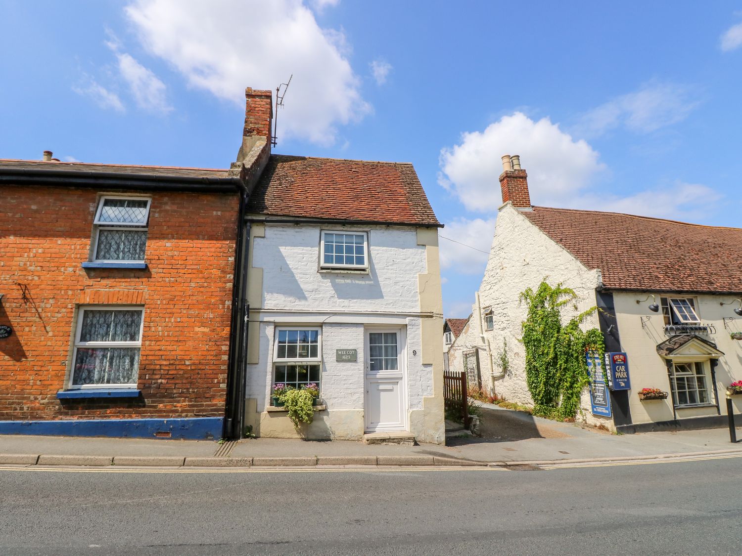 A street view of three connected houses with brick and white walls along a road at Wee Cot in Brading near Sandown