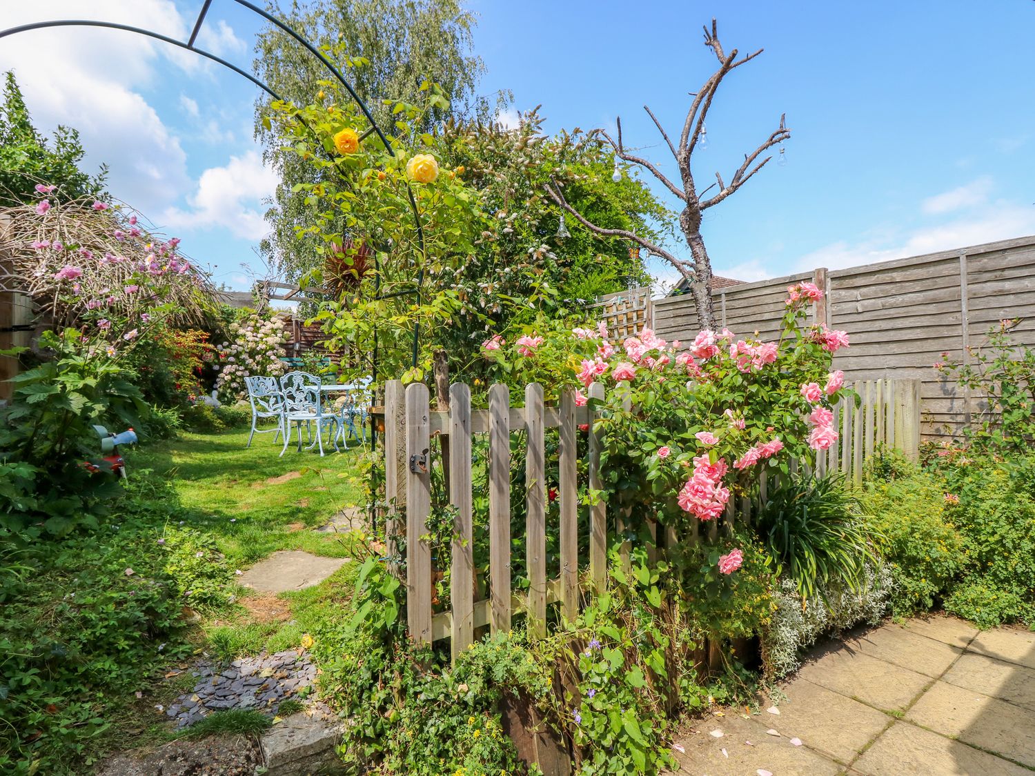 A garden with a wooden gate pink and yellow flowers and white garden furniture at Wee Cot in Brading near Sandown