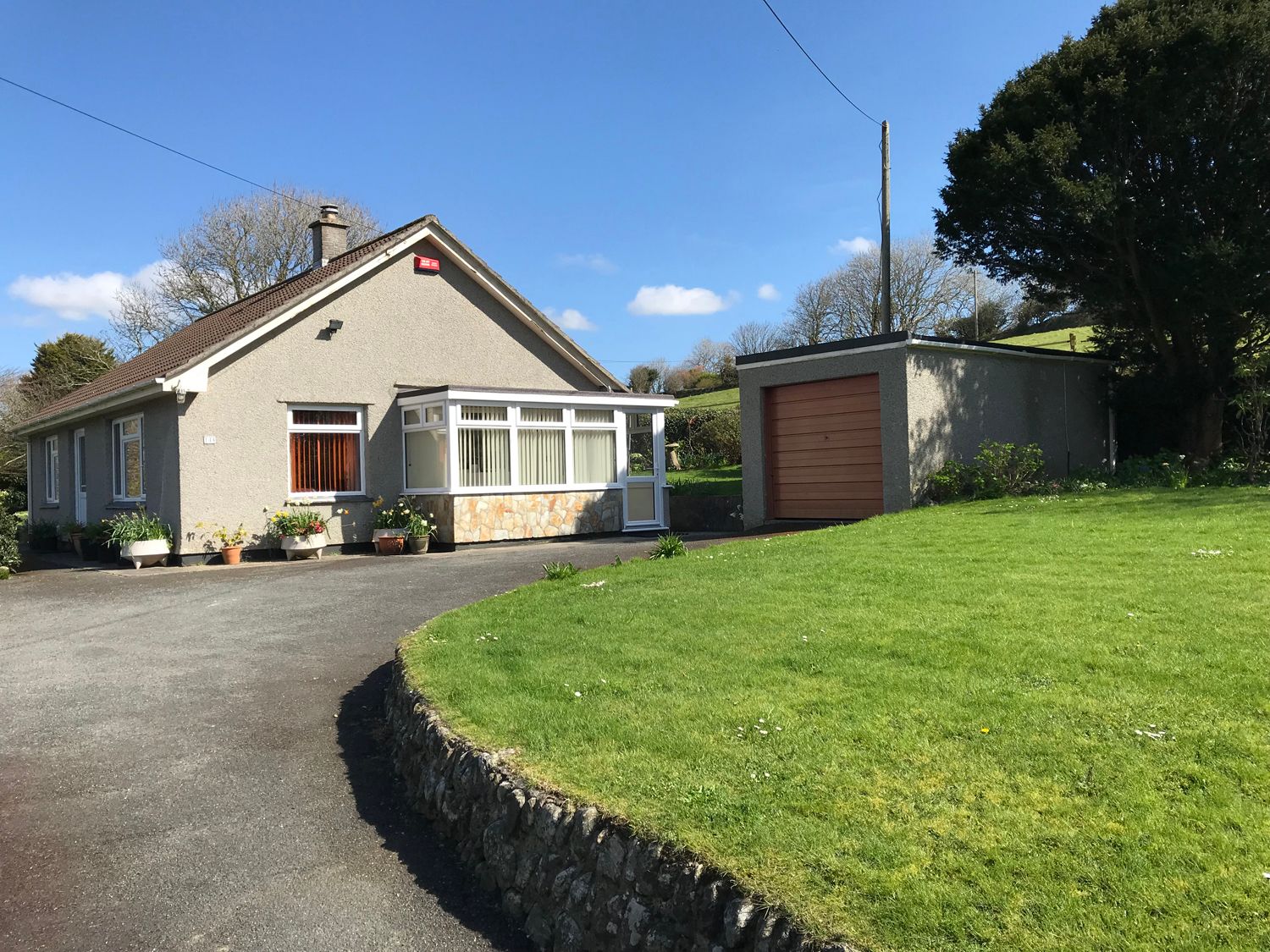 A single-story house with a driveway and a detached garage next to a grassy lawn at Trelowarth in St Agnes