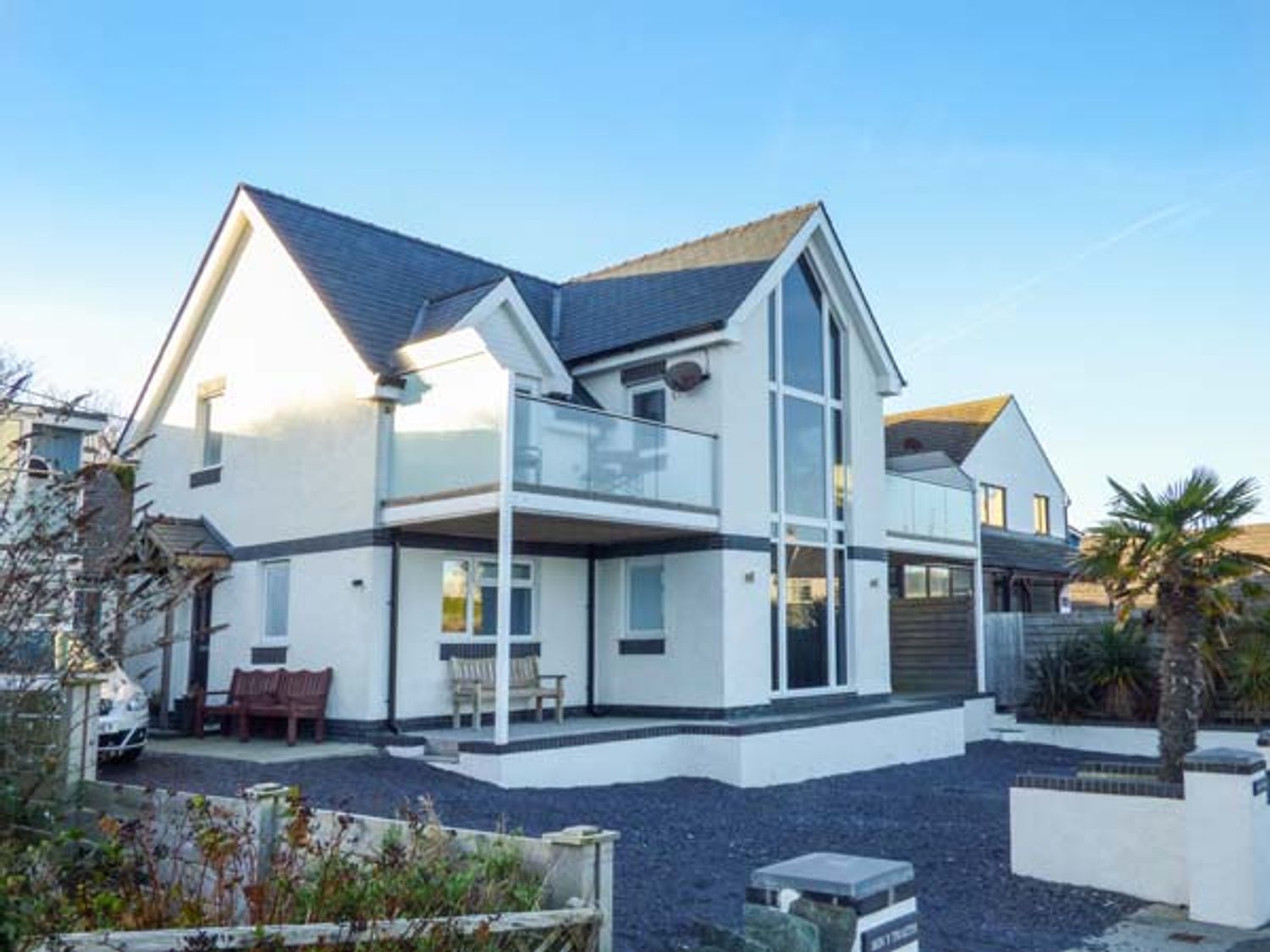 A two story house with glass balconies and benches outside at Glan Y Mor in Bull Bay
