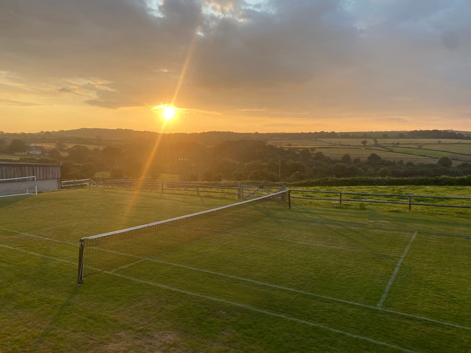An outdoor grass tennis court with a net at sunset in a rural area with fields and hills at Dexter in Treverva near Constantine