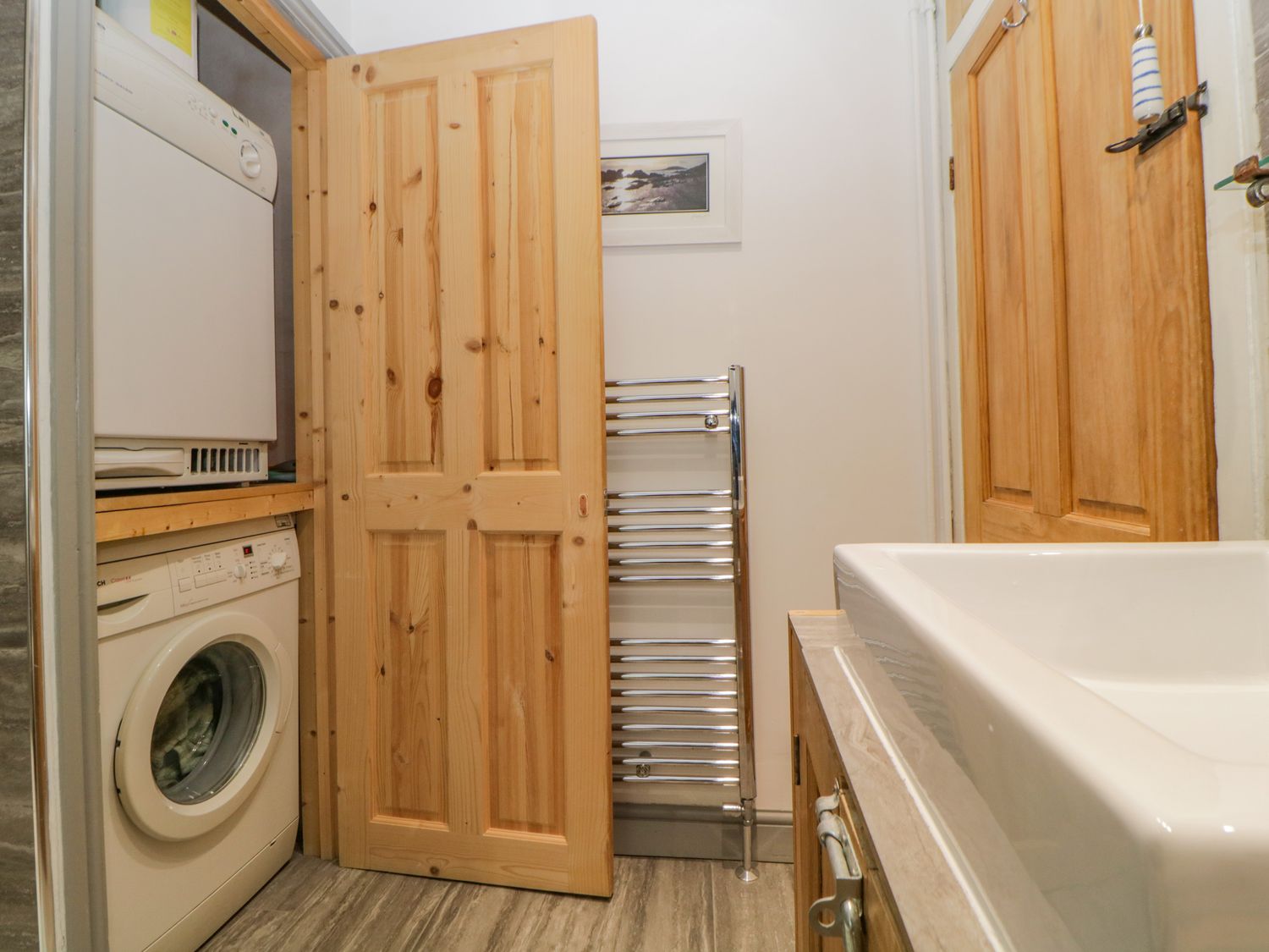 A laundry area with a washing machine and dryer behind wooden doors next to a sink and towel rack at Curlews Cottage in Looe