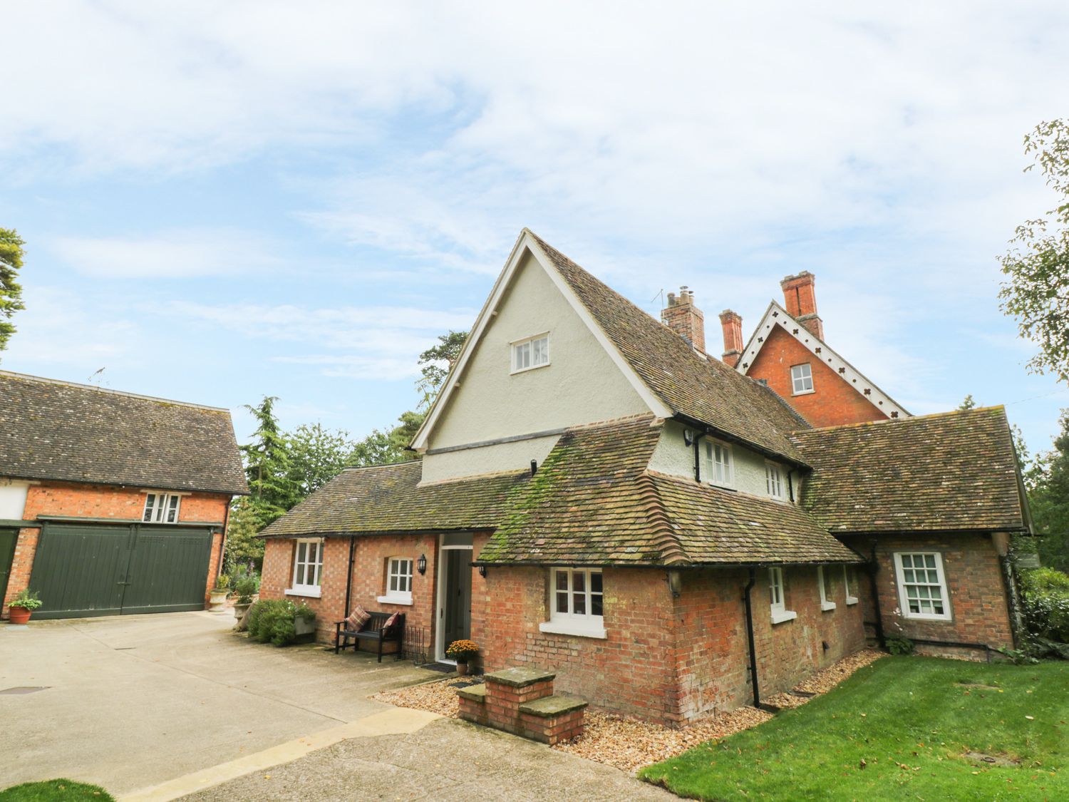 A brick house with multiple pitched roofs and a driveway with a bench at The Dower House in Sharnbrook