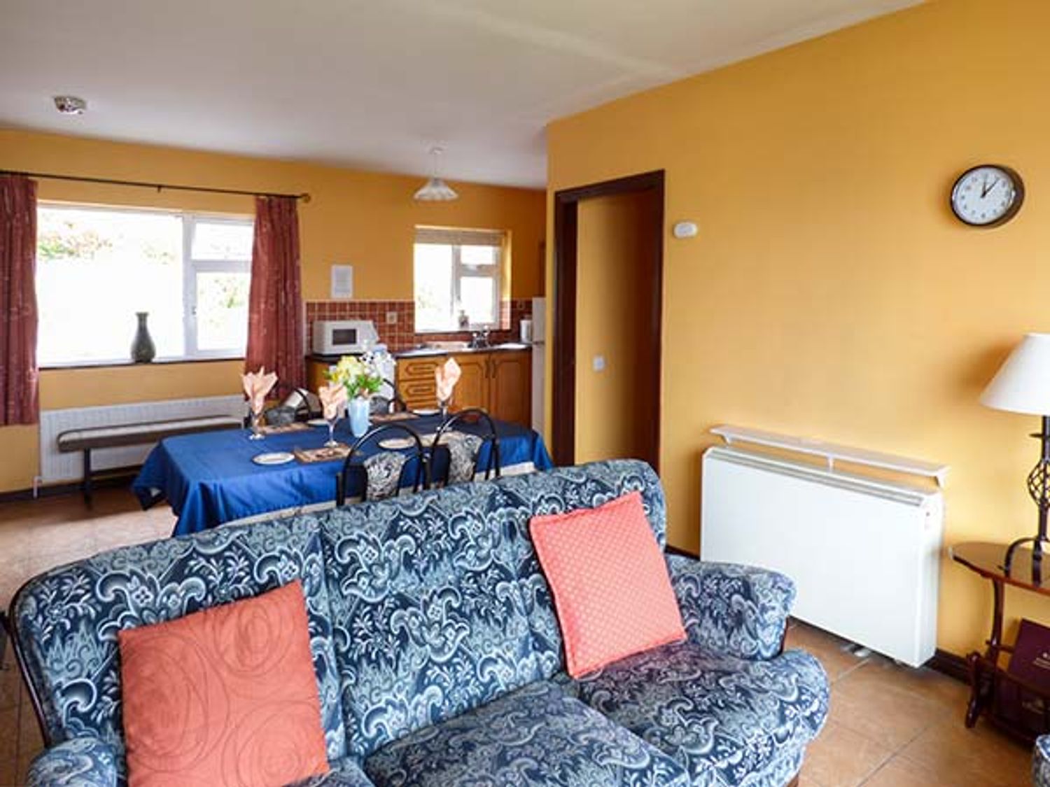 A living room with a patterned blue sofa and orange pillows and a dining table with a blue tablecloth at Rossbeigh Beach Cottage No 6 Rossbeigh near Glenbeigh County Kerry