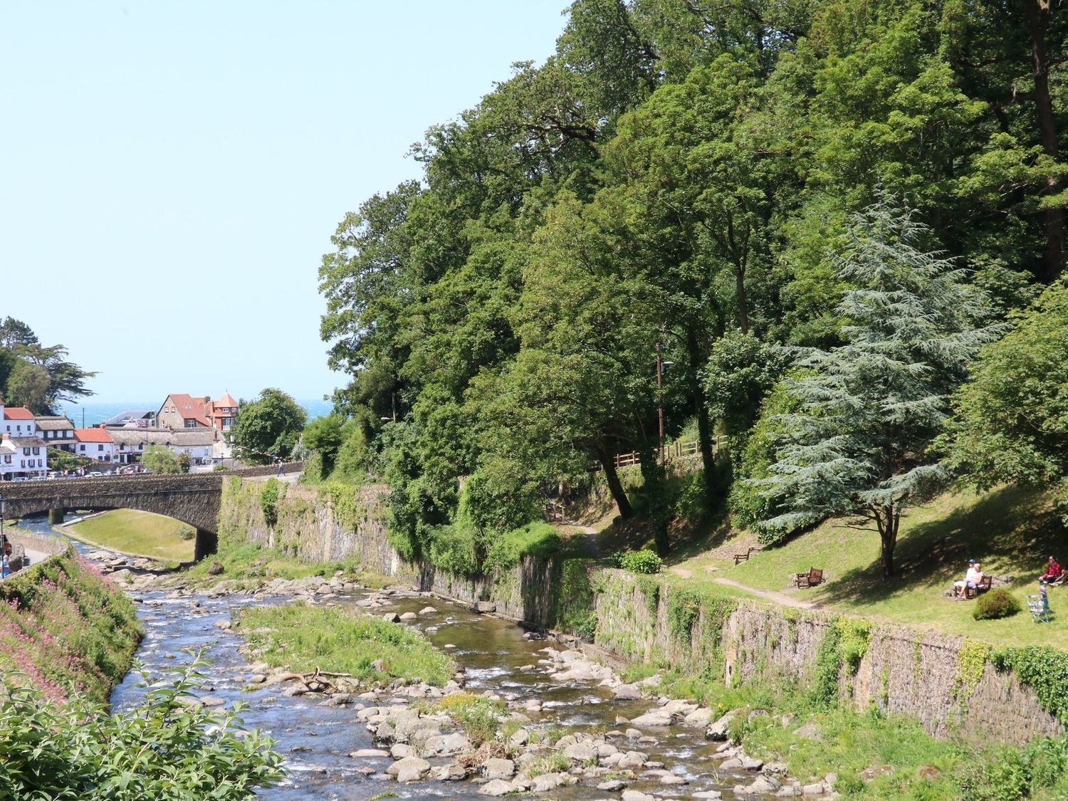 A river flowing under a stone bridge with trees and benches along the riverbank at Clooneavin Apartment 6 in Lynmouth near Lynton
