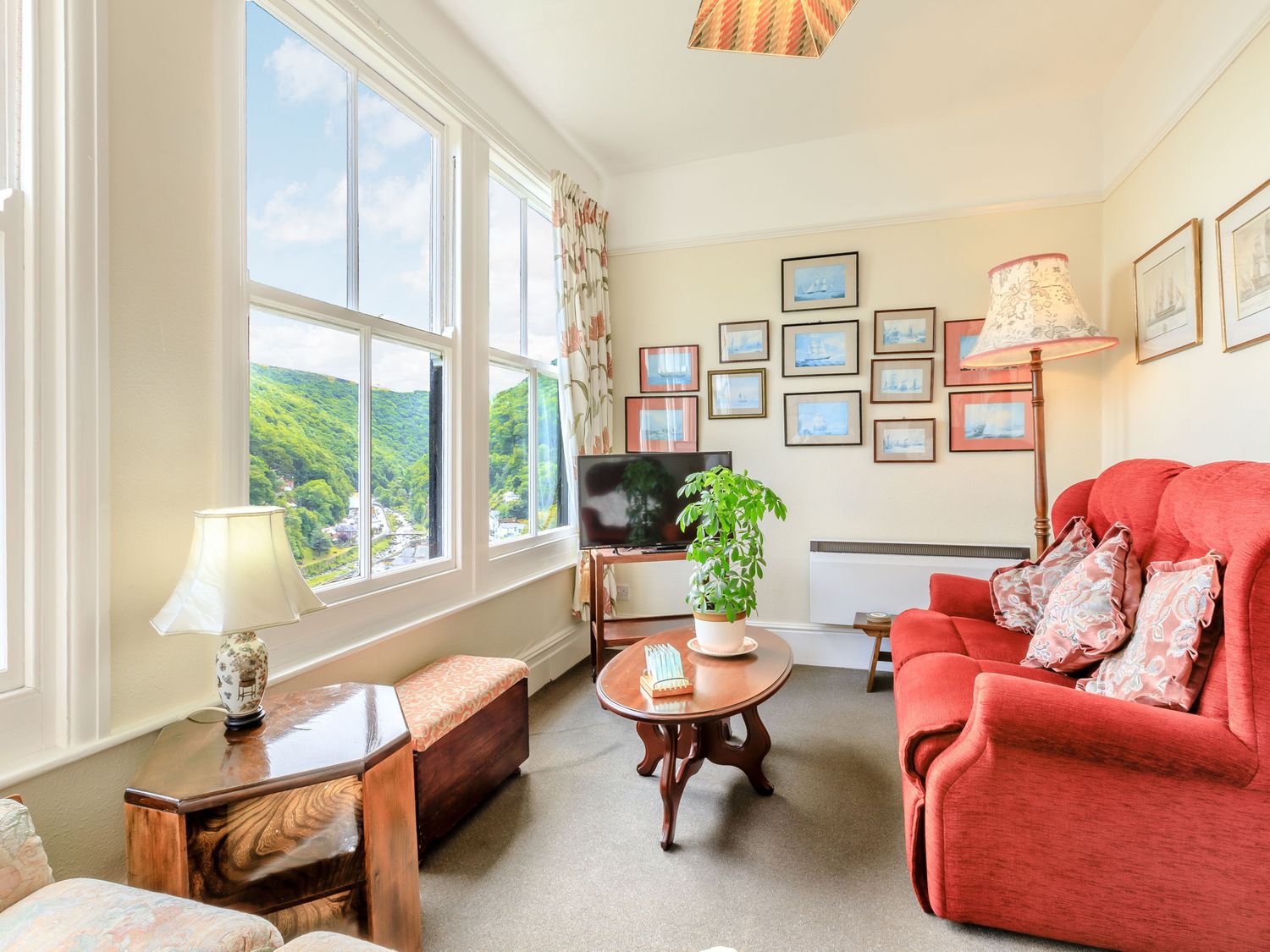 A sitting room with a red sofa and cushions a coffee table with a plant a television and framed pictures on the wall at Clooneavin Apartment 6 in Lynmouth near Lynton