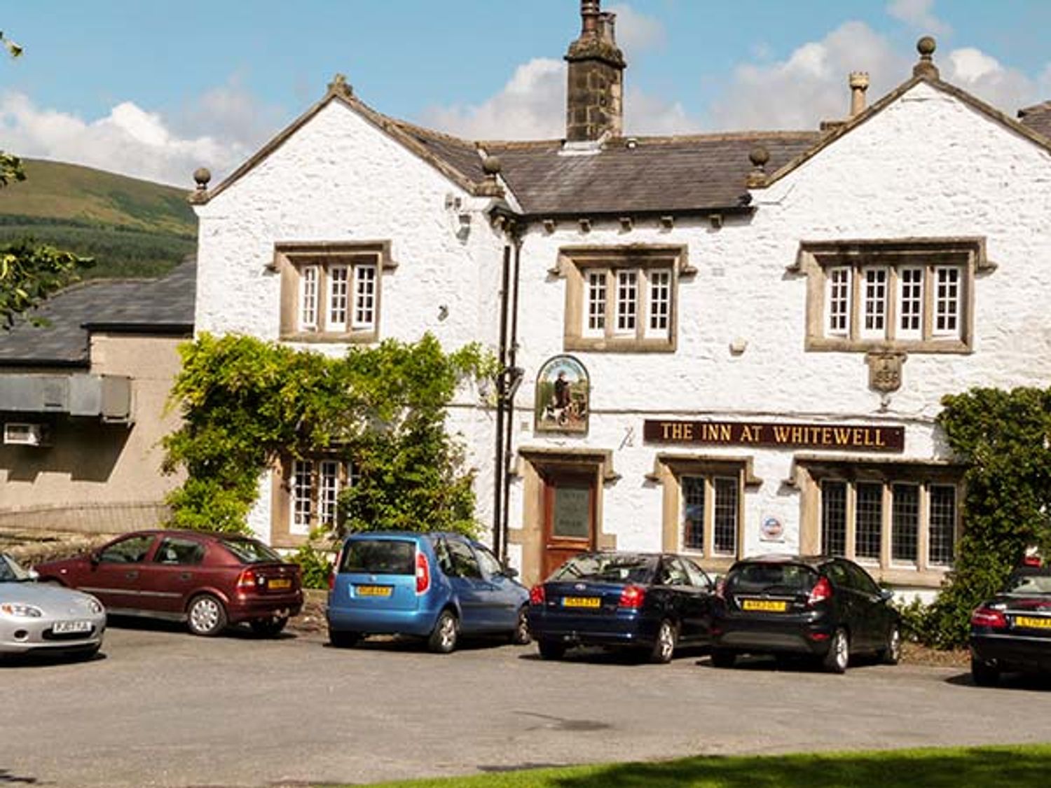 White building with multiple windows and cars parked in front at The Inn at Whitewell in Scorton