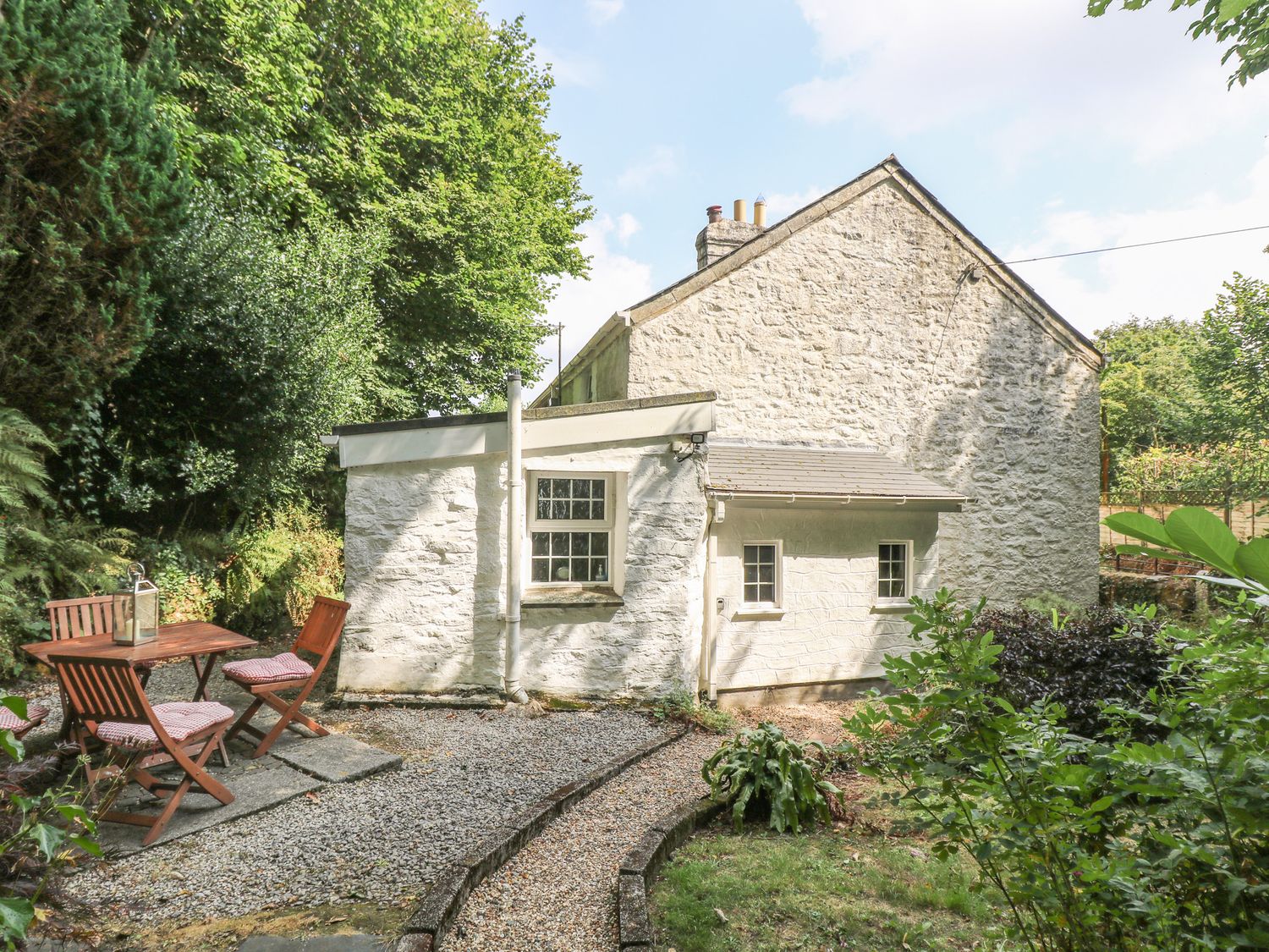 An outdoor seating area with a table and chairs beside a stone house with greenery around at Tinners Cottage in Liskeard