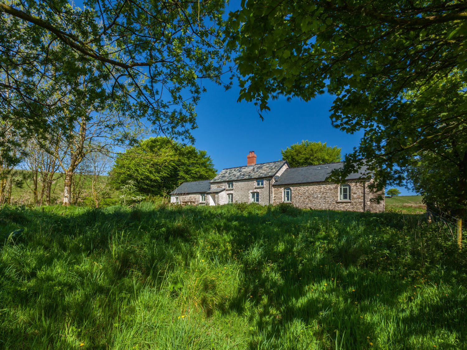 A stone house with slate roof surrounded by grass and trees at Limecombe in Simonsbath
