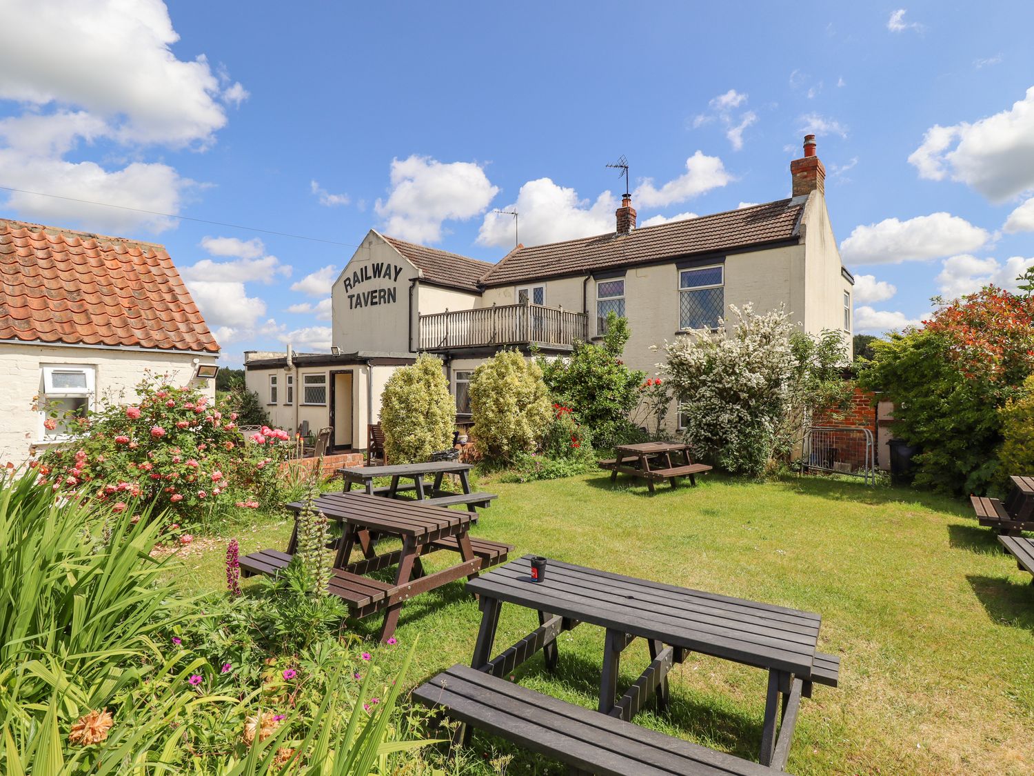 An outdoor seating area with picnic tables and garden plants in front of a building labeled Railway Tavern