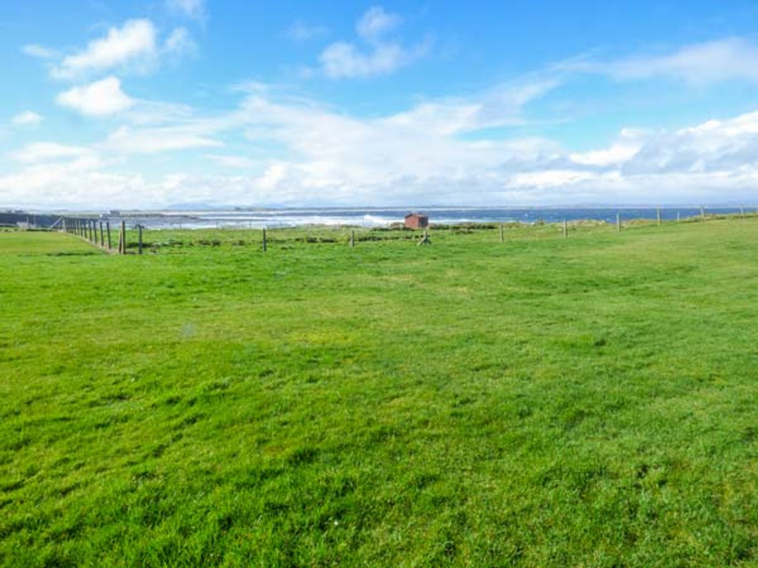 A green grassy field with a small shed near the coastline and blue sky at Sunset Beach Cottage in Enniscrone County Sligo