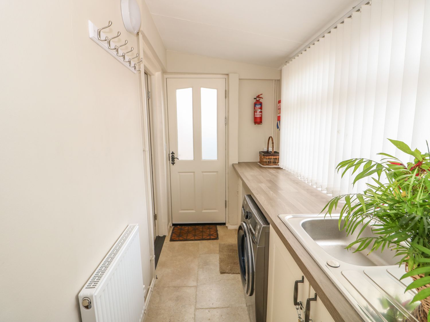 A laundry room with a washing machine sink and plant near a door at Bertelle Grimston