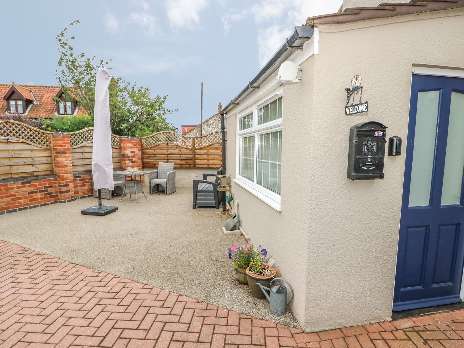 An outdoor patio area with a table and two chairs an umbrella closed near a beige house with a blue door and a black mailbox at Bertelle Grimston