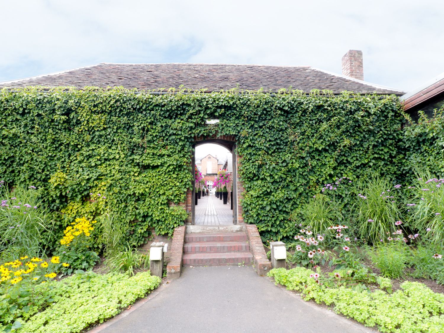 A garden entrance with ivy-covered walls and flower beds leading to a brick pathway at Town Mill in Bewdley