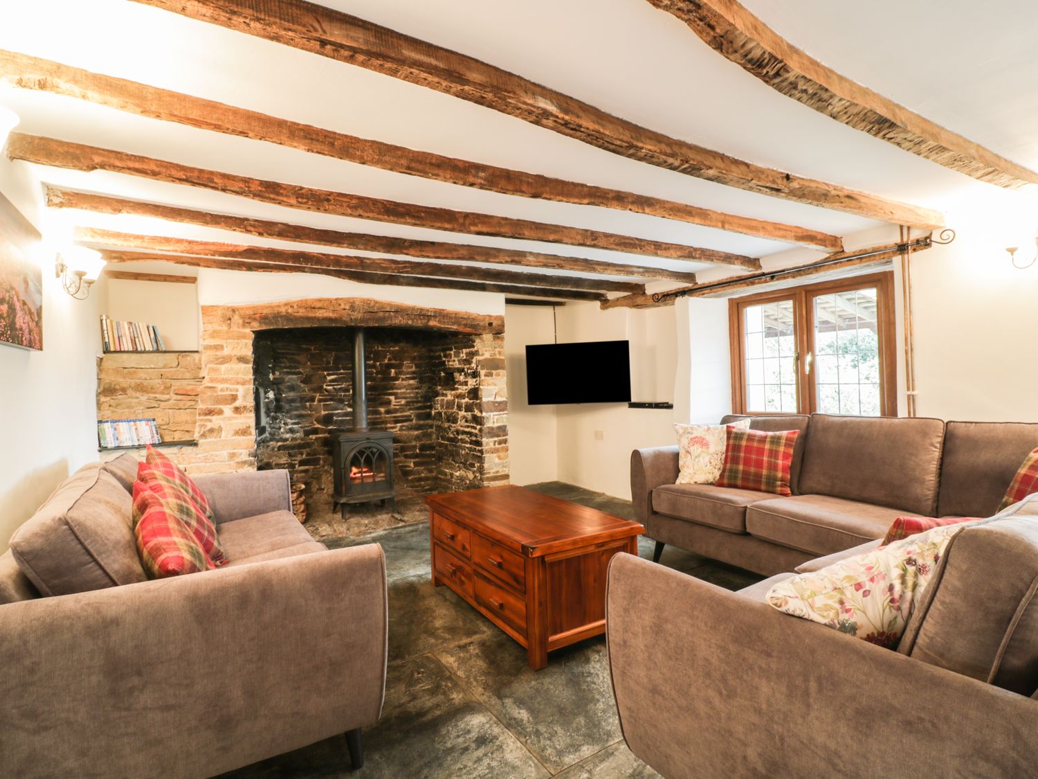 A living room with exposed wooden beams stone fireplace with wood burner sofas and a wooden coffee table at Lower West Curry Farmhouse in Launceston