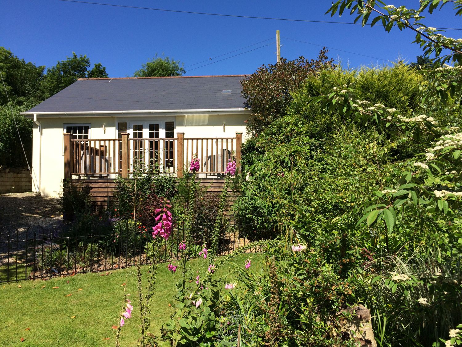 A small house with a wooden deck surrounded by a garden and green plants at The Coach House in Bodmin