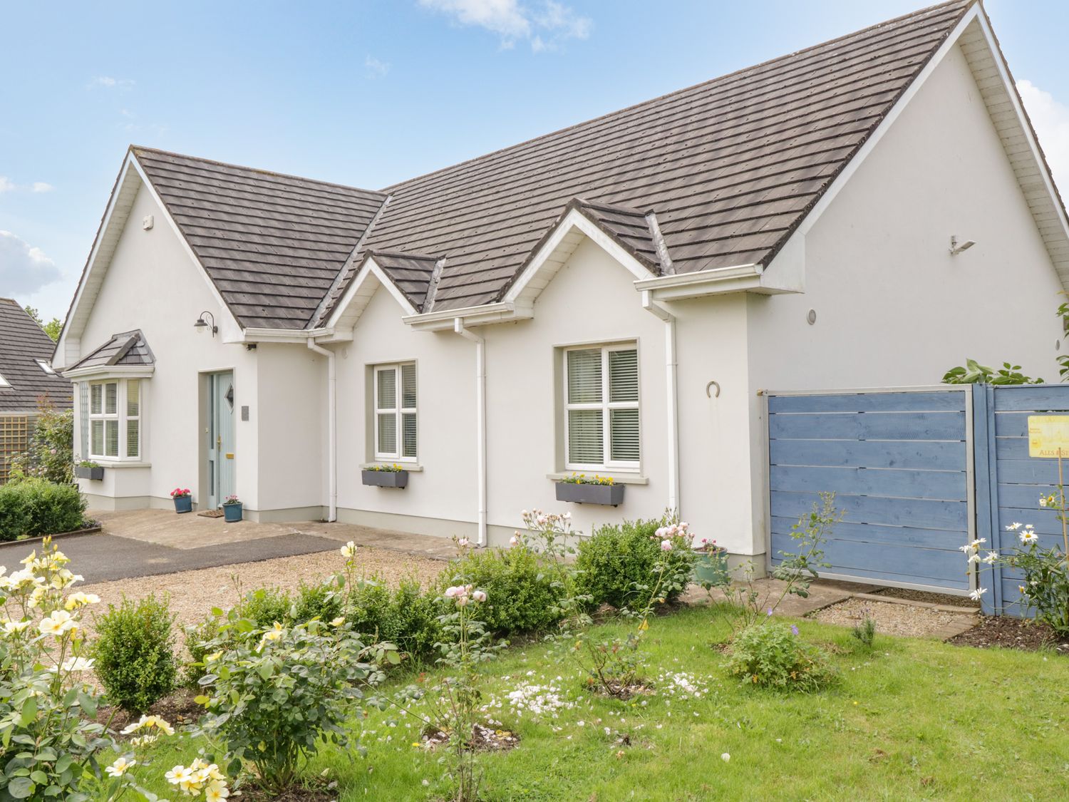 A white house with a grey roof a blue front door and flower beds in a garden at 2 Castle Cove in Dromahair County Leitrim