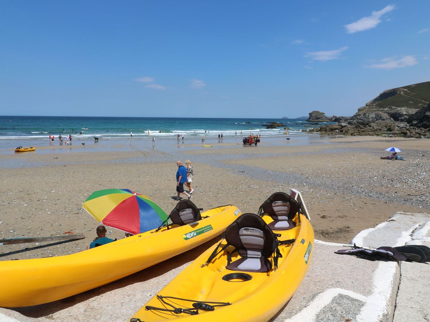 Two yellow kayaks on a sandy beach with people walking and the ocean in the background at Ocean Blue in Porthtowan