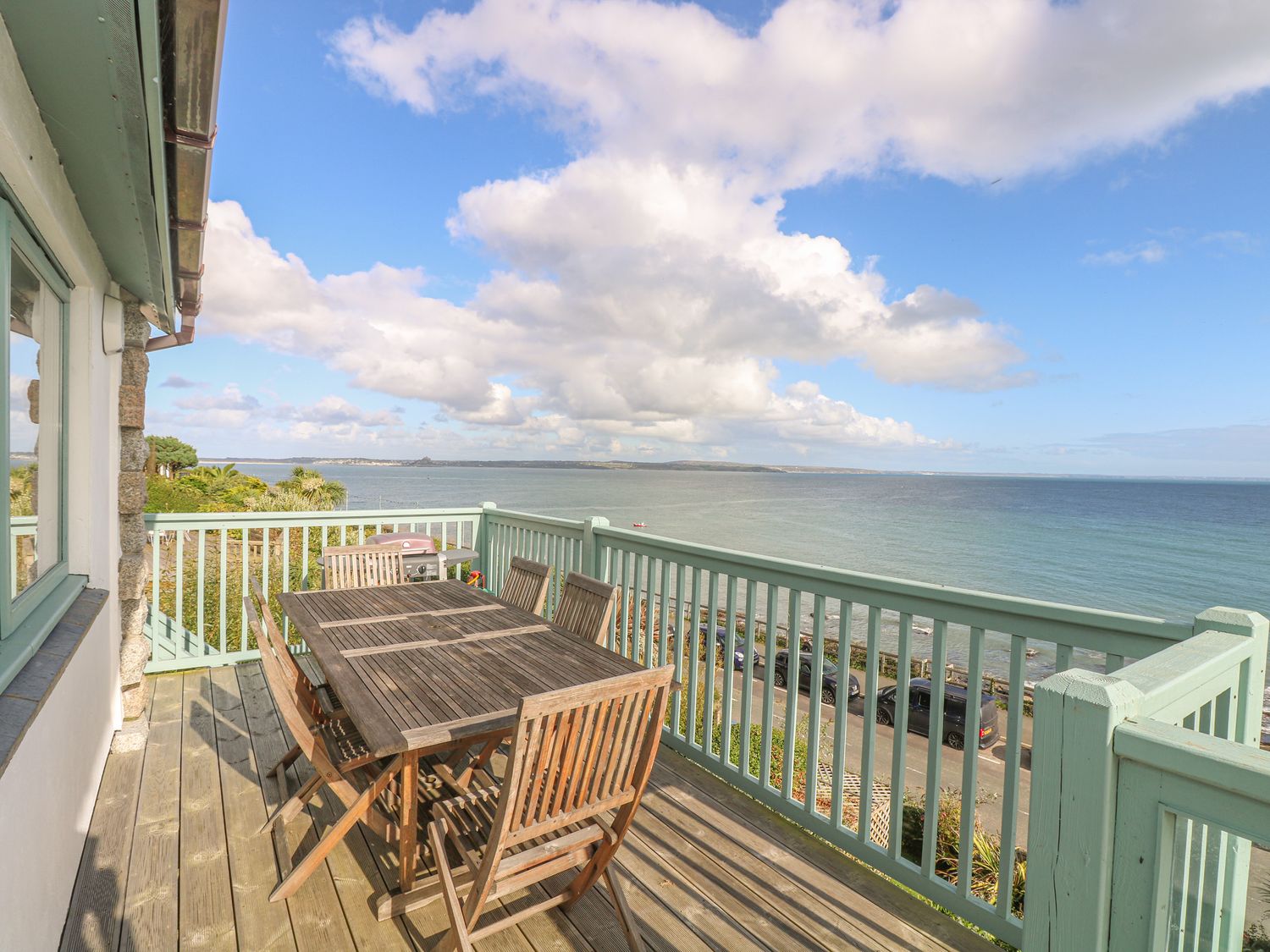 A wooden deck with a table and chairs overlooking the sea at Harbour Lights in Mousehole