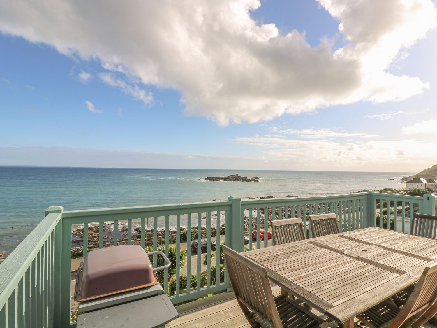 A balcony with a wooden table and chairs and a barbecue overlooking the sea at Harbour Lights in Mousehole