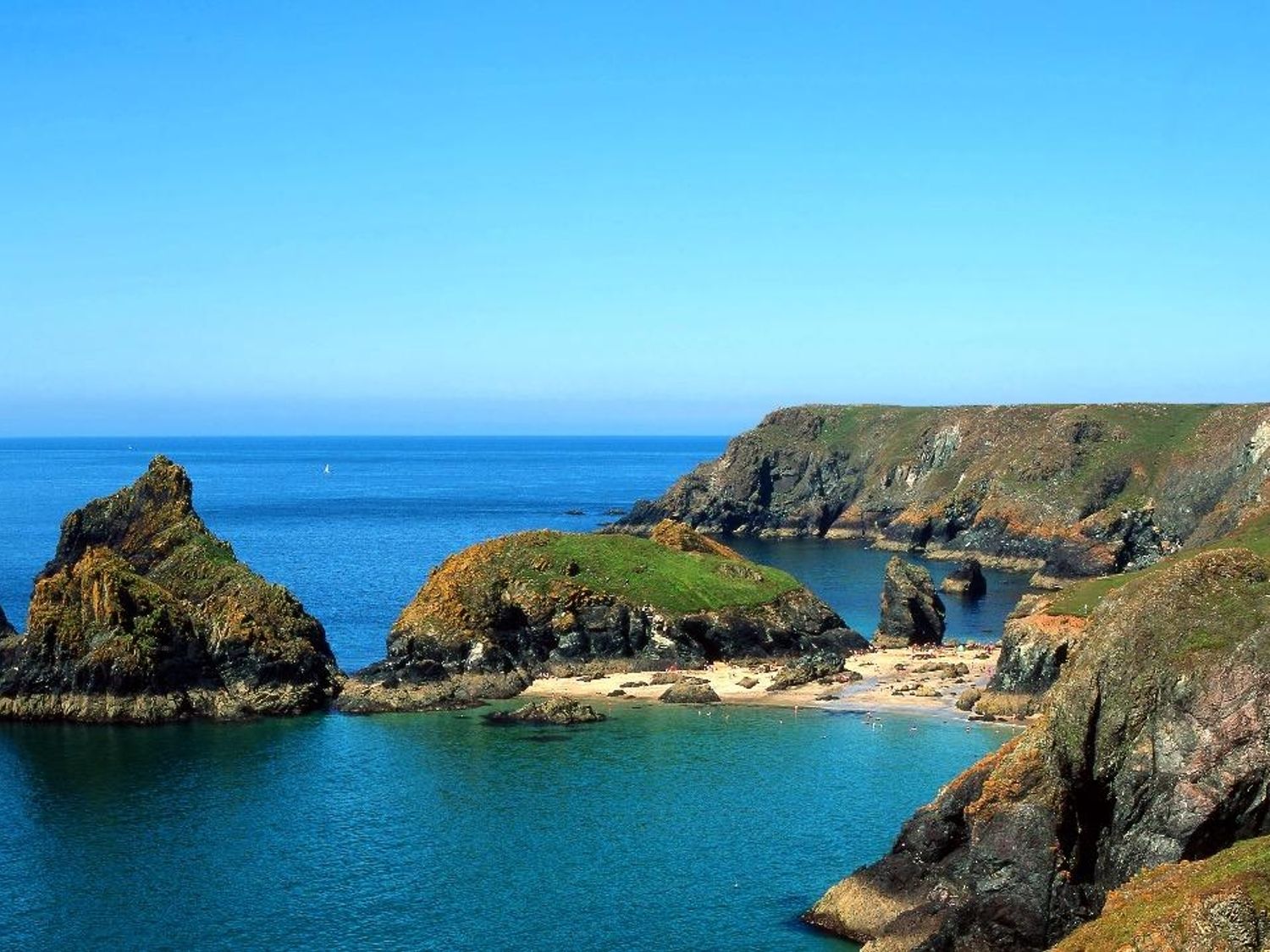 Rock formations and cliffs around a small sandy cove with clear blue sea at Penrose Farm Cottage in St Keverne
