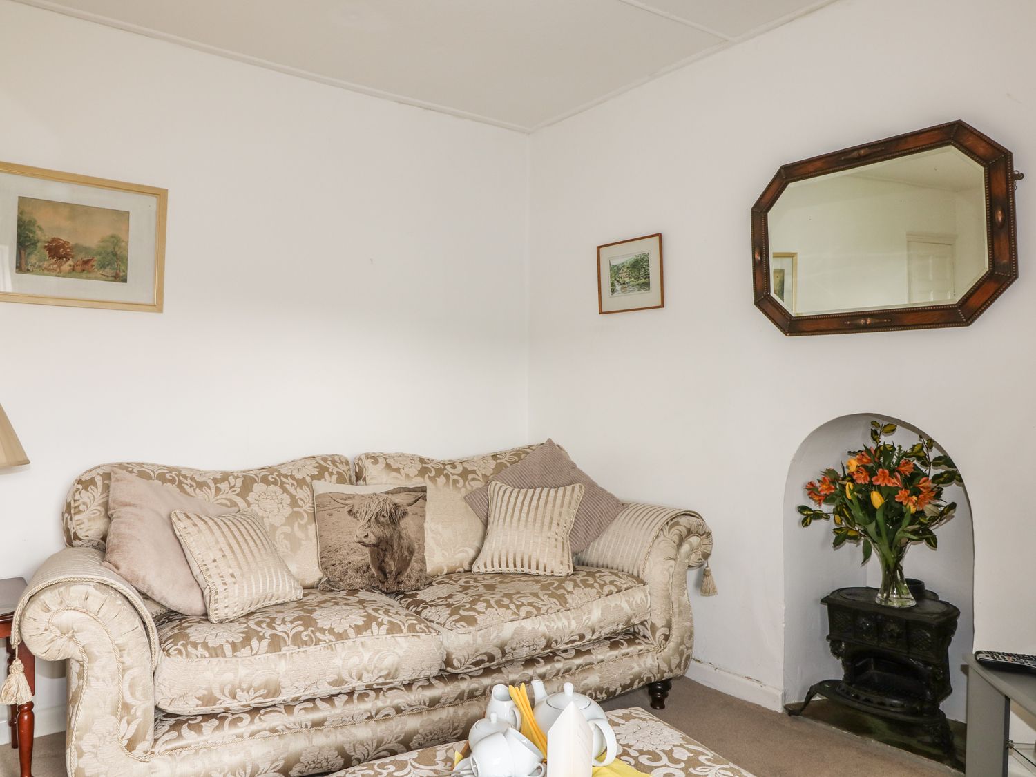 A living room with a patterned sofa pillows flowers in a niche and a mirror on the wall at Penrose Farm Cottage in St Keverne
